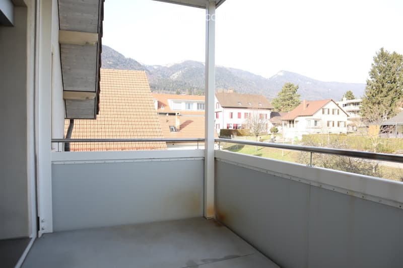 Balcony with metal railing, overlooking a residential area with houses and mountains in the background.