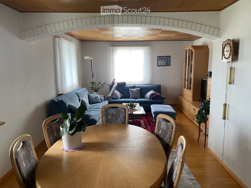 Bright living and dining area with a blue sofa, ottoman, coffee table, dining table with chairs, and a cabinet with glass doors.