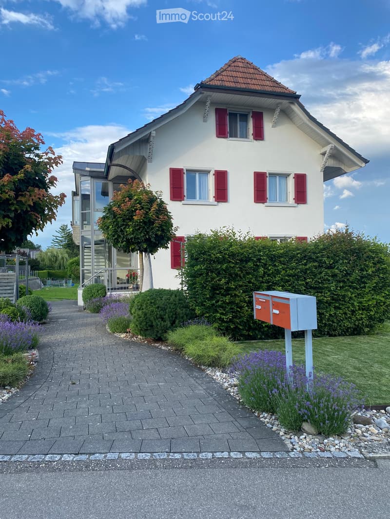 Two-story white house with red shutters, surrounded by well-maintained garden and pathway.