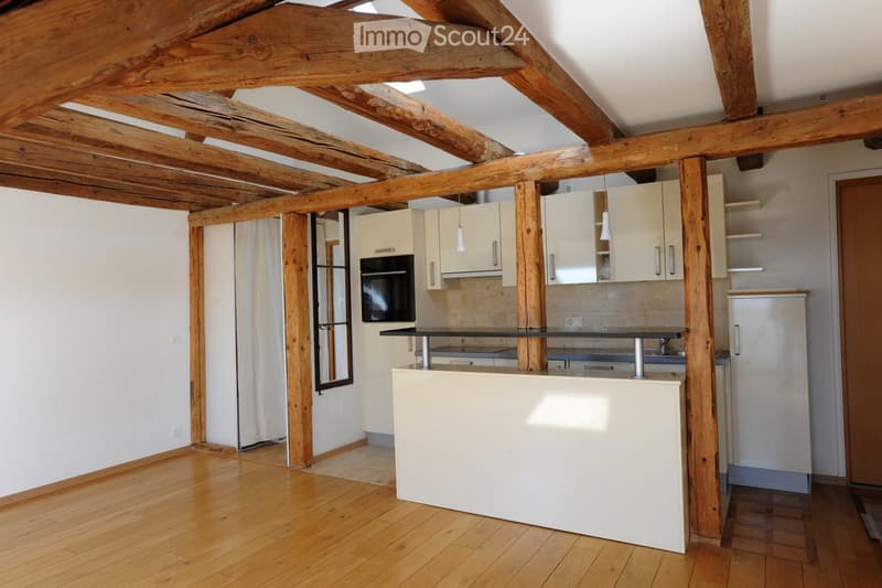 Bright kitchen with wooden beams, white cabinets, a microwave, and a counter. The space features wooden flooring and exposed wooden beams on the ceiling.