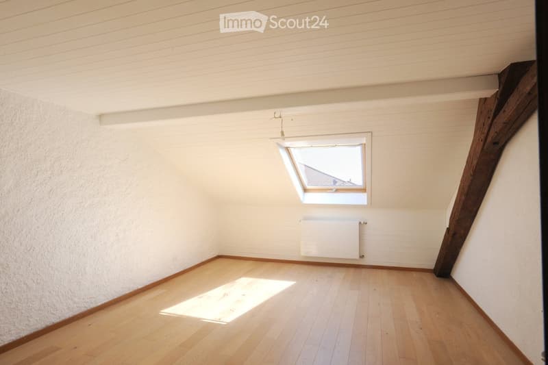 Empty attic room with wooden flooring, white walls, and a skylight window. No furniture or equipment present.
