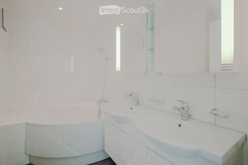 Modern bathroom with white tiles, a bathtub, two sinks, and a mirrored cabinet.
