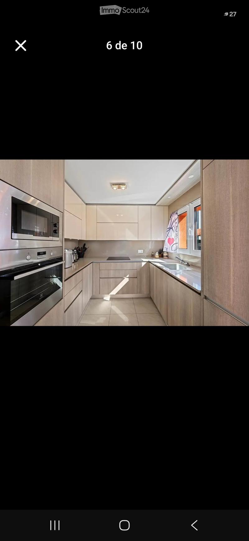 Modern kitchen with light wood cabinets, stainless steel appliances, and a large window with a decorative curtain.