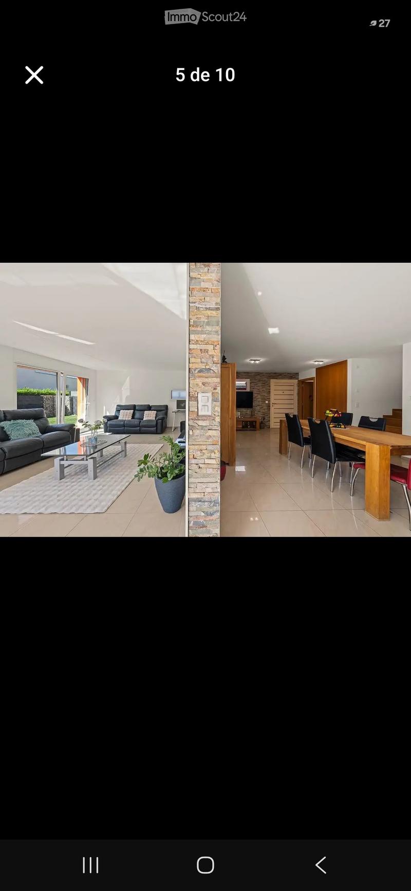 Modern living and dining area with a sofa, coffee table, dining table, and chairs. The space features a mix of contemporary and rustic elements, including a stone accent wall and large windows allowing natural light to fill the room.
