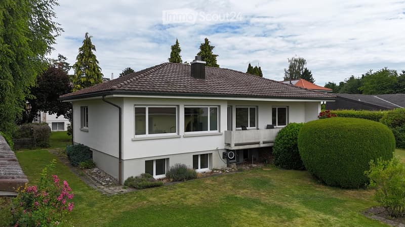 Single-story house with white exterior, tiled roof, multiple windows, and a small balcony on the right side.