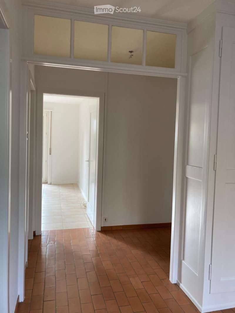Empty hallway with tiled floors, white walls, and multiple doors leading to other rooms.