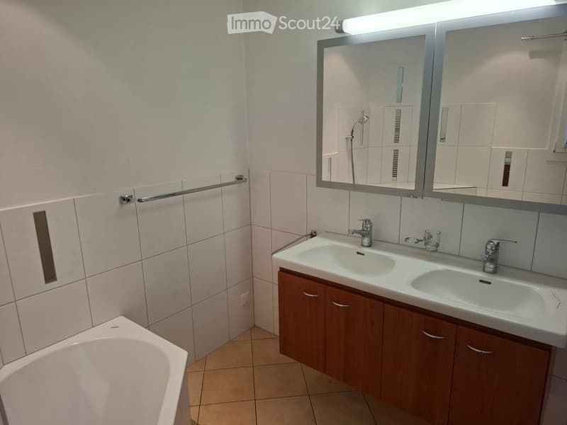 Modern bathroom with double sink, large mirror, wooden cabinet, and bathtub.