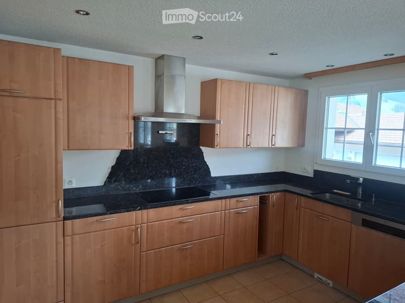 Modern kitchen with light wooden cabinets, granite countertops, built-in range hood, and stainless steel sink and dishwasher.
