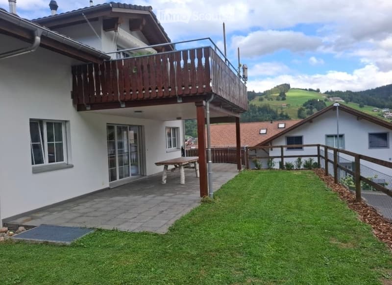 A well-maintained garden area with a wooden bench, a paved patio, and a wooden balcony overlooking a scenic countryside view.