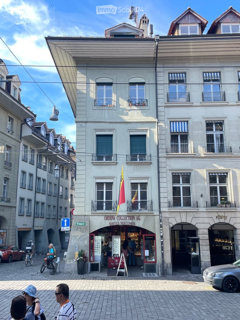 A multi-story building with a storefront labeled "ORDONA COLLECTION AG SWISS WATCHES" and several windows with balconies. The building has a classic architectural style with stone facades and decorative railings.
