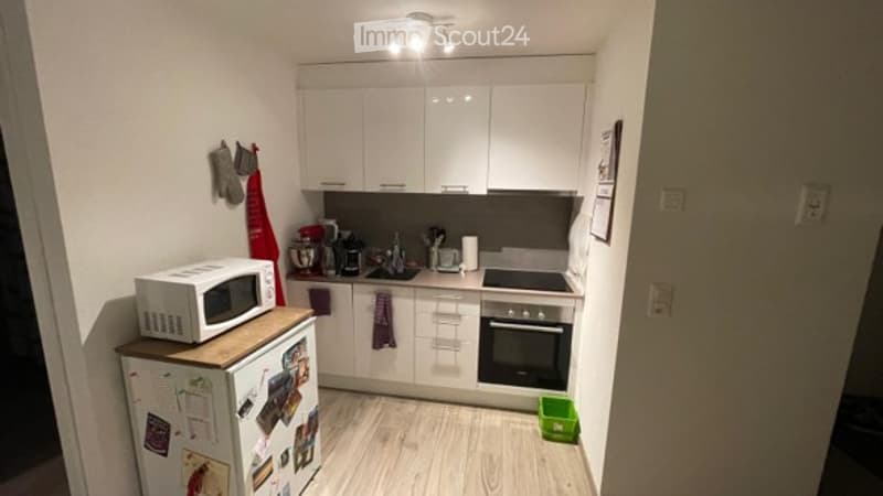 Modern kitchen with white cabinets, stainless steel appliances, and a wooden floor. Features a refrigerator, microwave, oven, stove, and various kitchen tools.