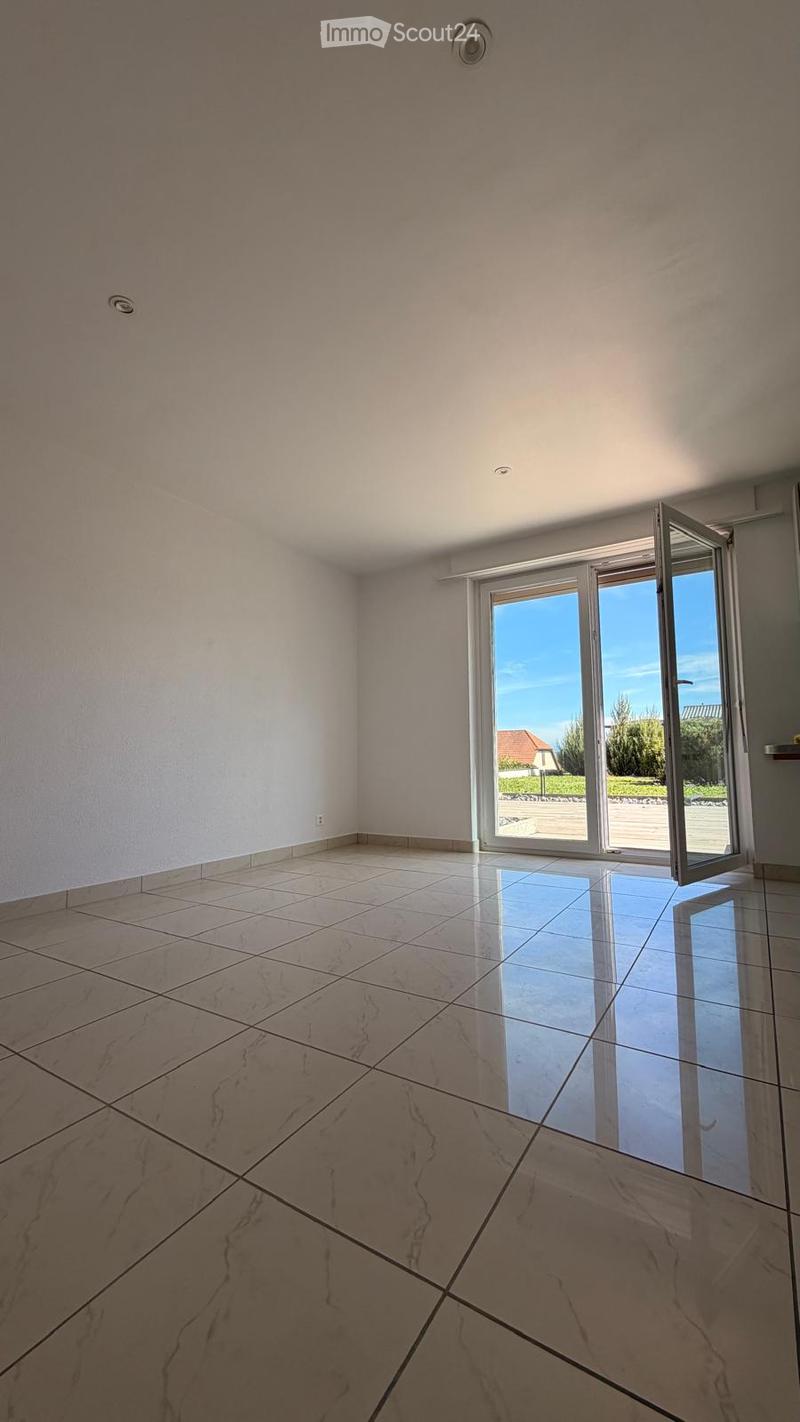Empty room with light-colored tiled flooring and white walls, featuring a large sliding glass door that opens to an outdoor area.
