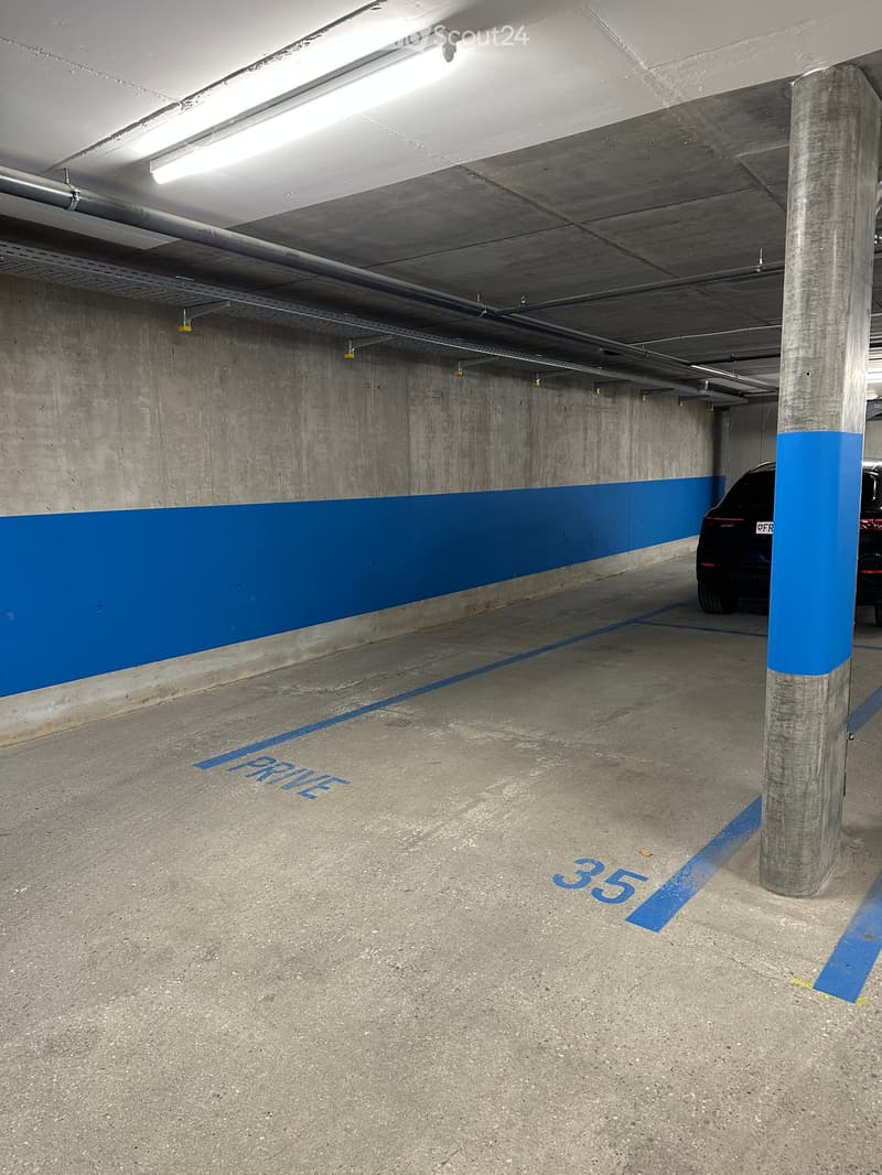 Underground parking area with concrete floors and walls, marked parking spaces, and a single car partially visible.