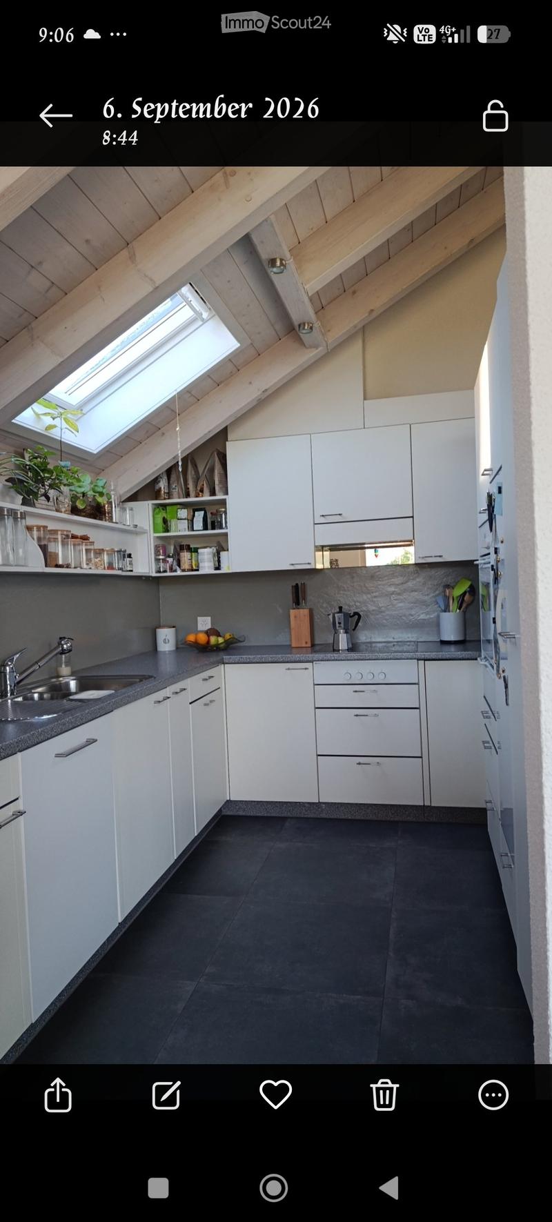 Modern kitchen with white cabinets, dark countertops, and a skylight window. Includes a sink, coffee maker, cutting board, bowl, and various kitchen items on shelves.