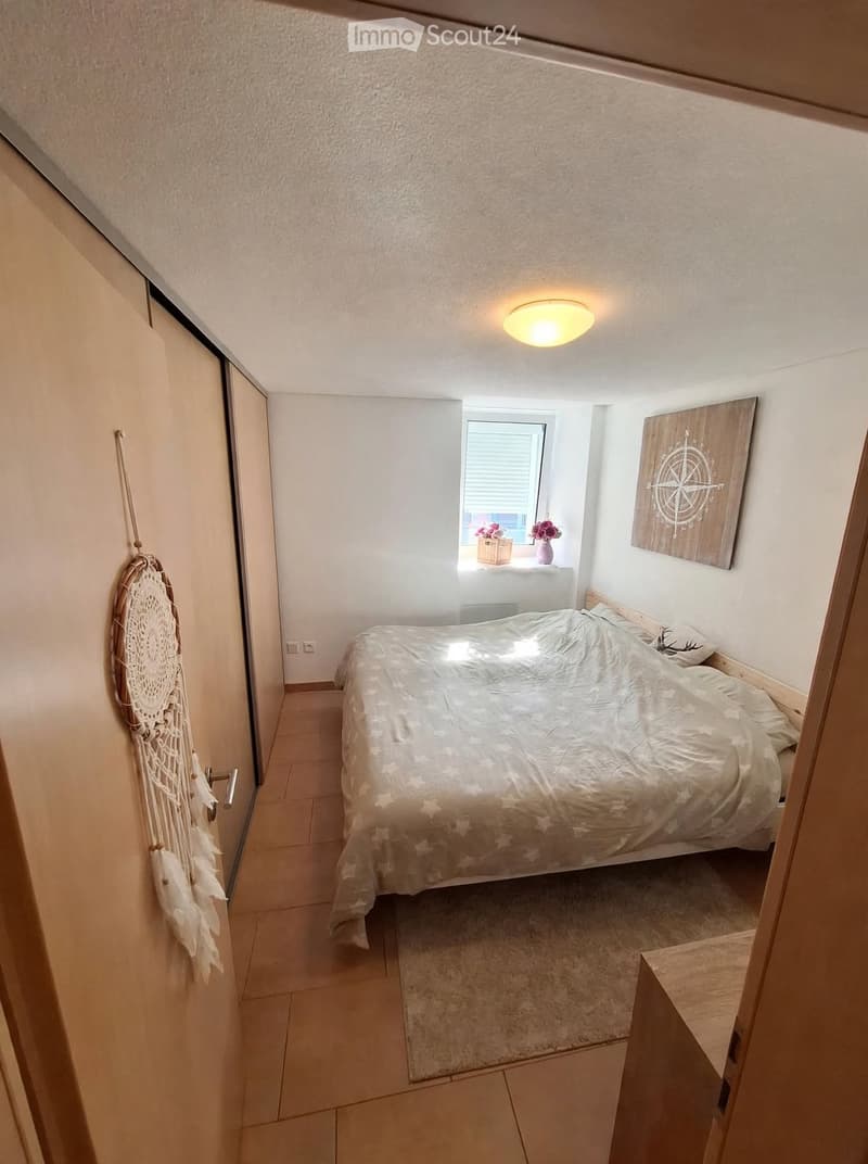 Cozy bedroom with a double bed, dreamcatcher on the wall, a picture frame, and a vase with flowers on the windowsill.