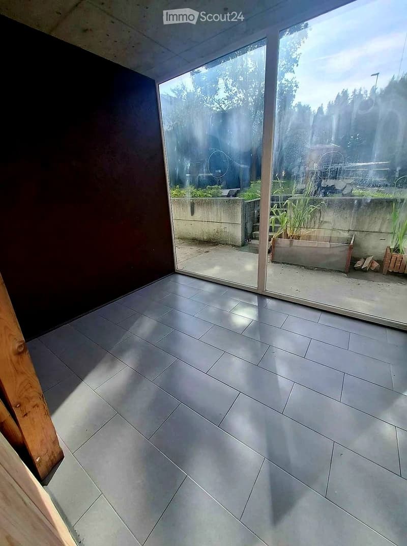 Modern indoor space with large glass sliding doors leading to a concrete patio area with plants and outdoor furniture.