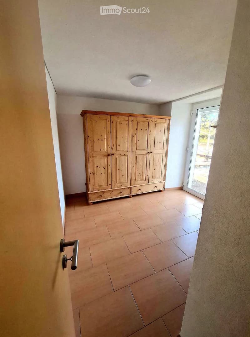 A hallway with tiled flooring, a wooden wardrobe, and a sliding glass door leading outside.