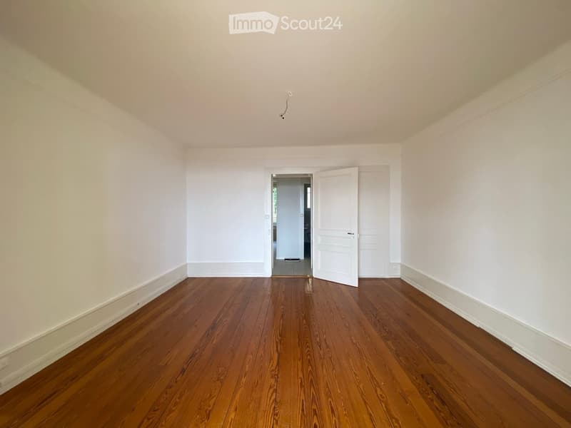 Empty room with wooden flooring and white walls, featuring a partially open door leading to another room.