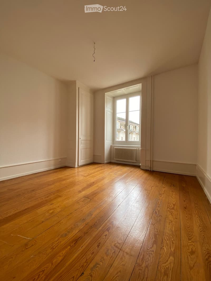 Empty room with wooden flooring, white walls, a single window with white frame, a white door, and a radiator below the window.