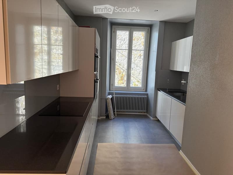 Modern kitchen with white cabinets, dark countertops, and a large window offering a view of the outside. The space includes a sink, oven, and a radiator below the window.