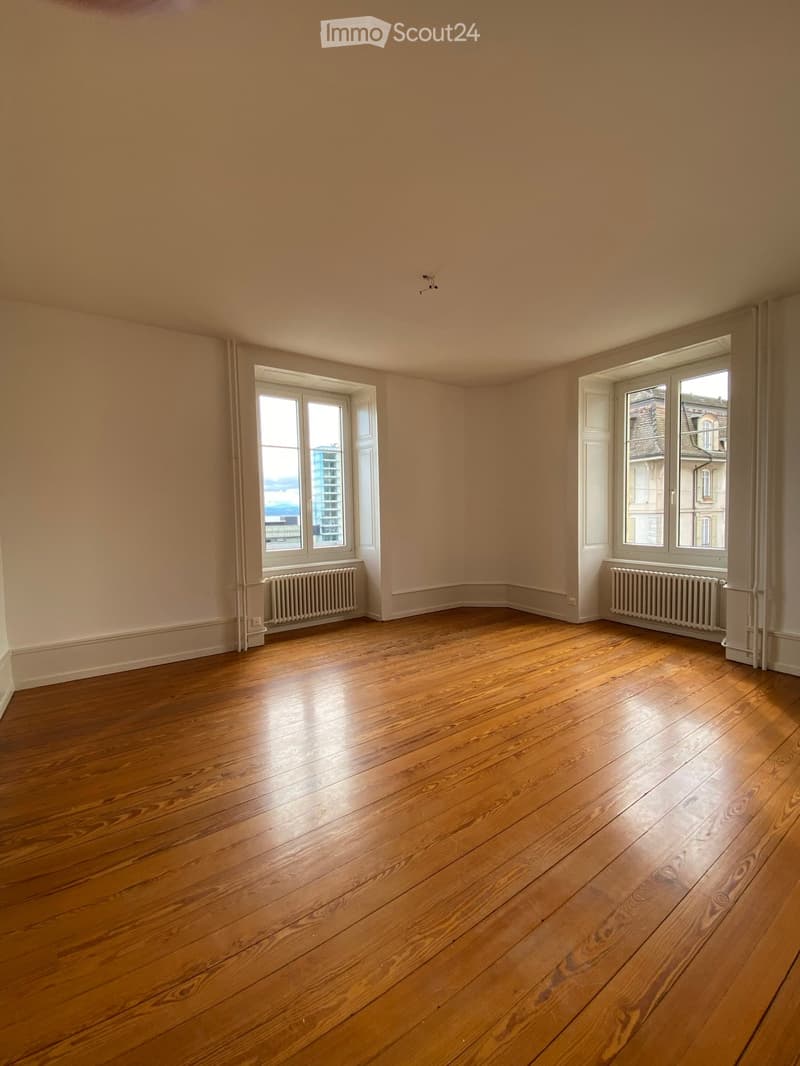 Empty room with wooden flooring, large windows, and radiators on both sides.