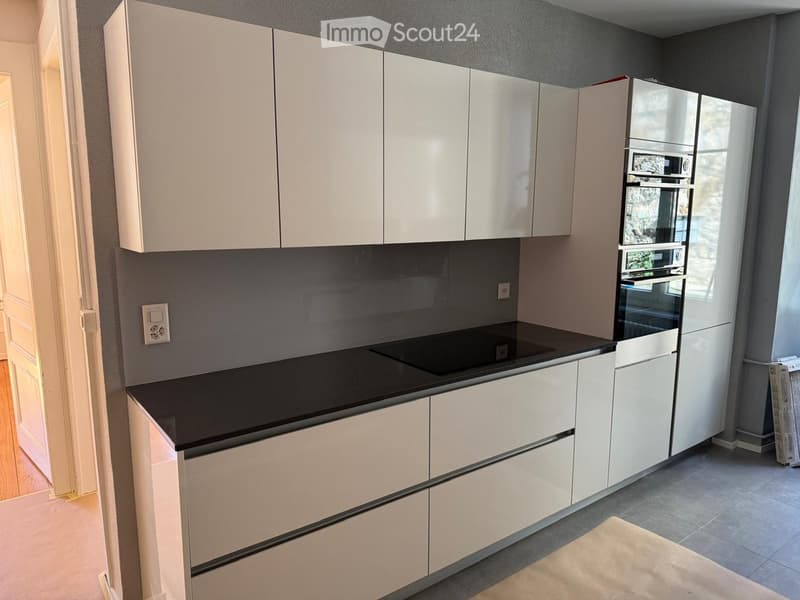 Modern kitchen with white cabinets, black countertop, induction cooktop, and stainless steel appliances.