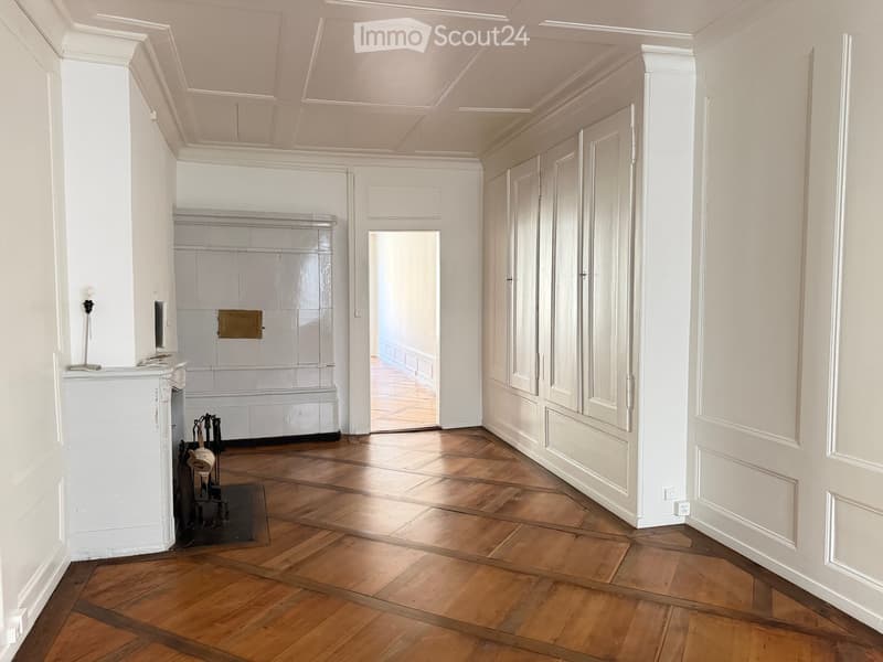 Elegant hallway with wooden herringbone flooring, white walls, ornate ceiling moldings, and a fireplace with a decorative mantel. Features built-in cabinets and a small table with a lamp.