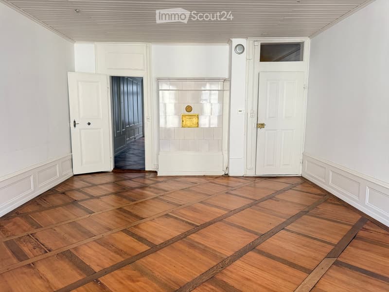 Empty room with wooden herringbone flooring, white walls, and several doors leading to other spaces.