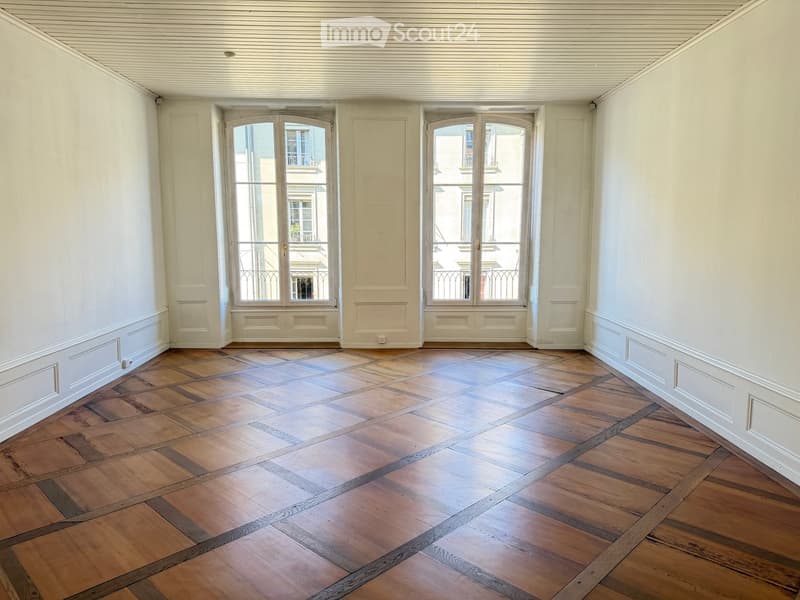 Empty room with wooden herringbone flooring, white walls, and large windows with metal railings leading to a balcony.