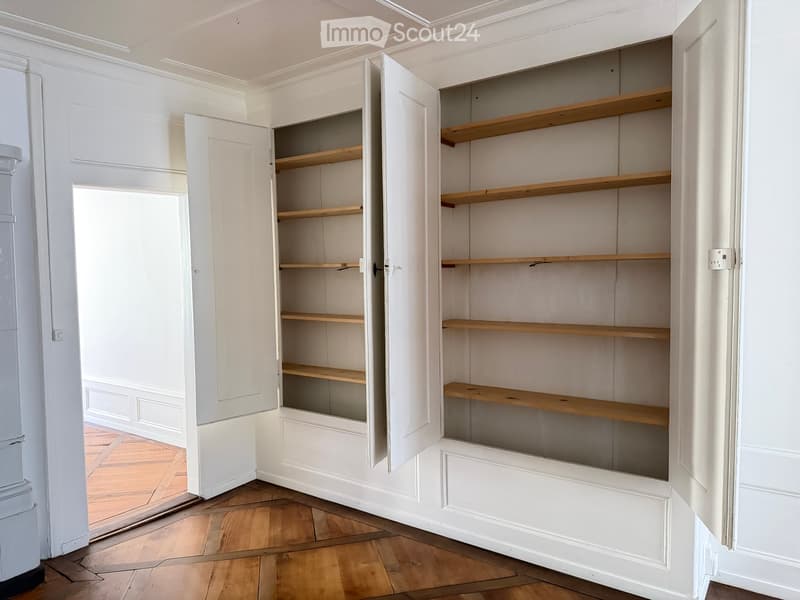 Empty room with built-in white cabinets and wooden shelves, featuring a wooden floor and white walls.
