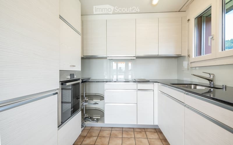 Modern kitchen with white cabinets, stainless steel oven, sink, and faucet, featuring a tiled floor and large windows.