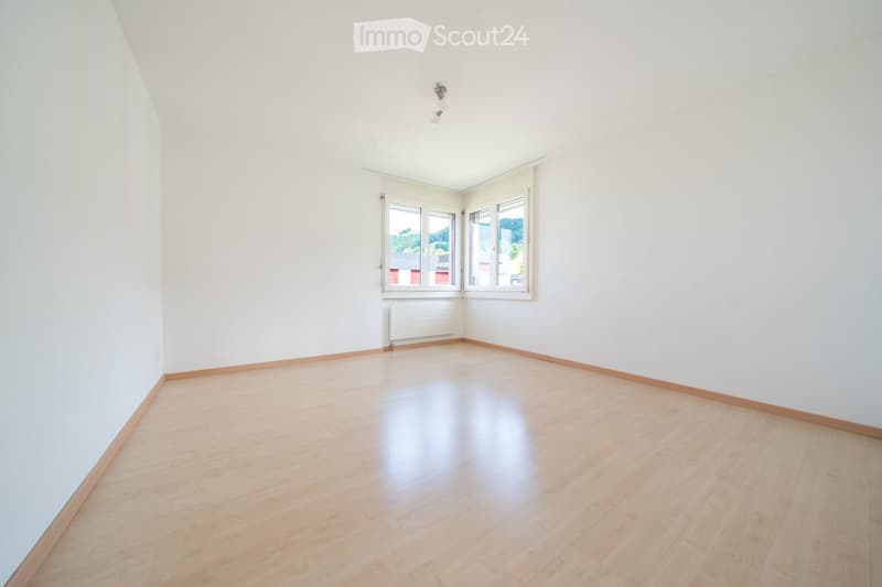 Empty room with light wooden flooring, white walls, and large windows with blinds. No furniture or equipment present.