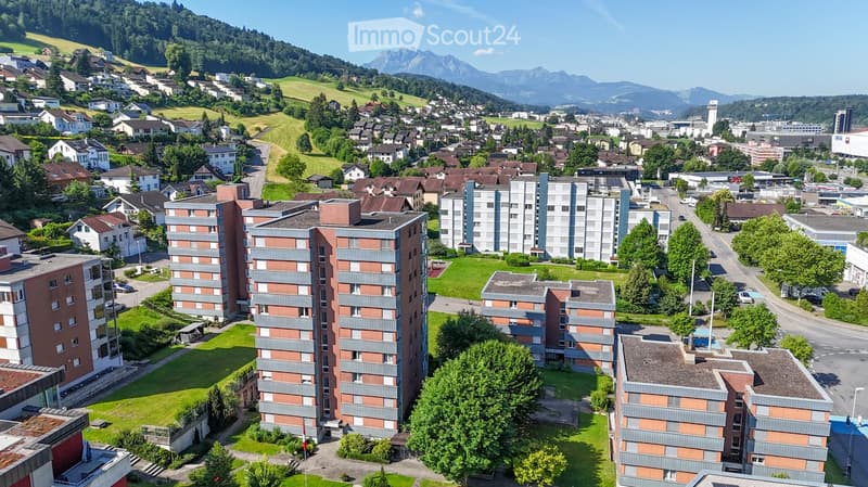 Aerial view of a residential area with multiple apartment buildings, green spaces, and surrounding mountains.
