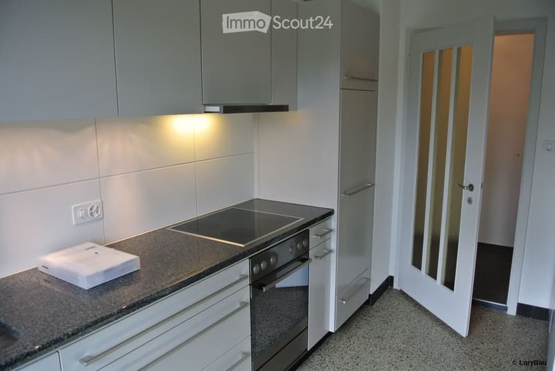 Modern kitchen with white cabinets, granite countertop, induction stove, and built-in oven. Features recessed lighting and a sleek design.