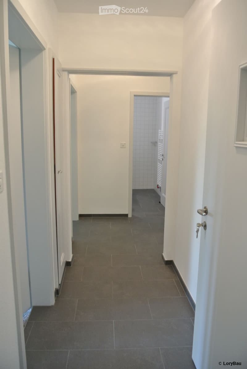 Empty hallway with white walls, grey tiled floor, and several doors leading to other rooms.