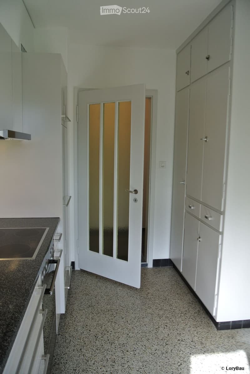 Modern kitchen with white cabinets, granite countertop, and induction stove. Open doorway leads to another room.