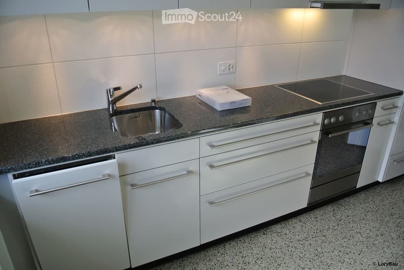 Modern kitchen with white cabinets, granite countertop, stainless steel sink, and built-in appliances including an oven and induction cooktop.