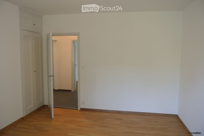 Empty room with wooden flooring, white walls, and a partially open door leading to another room.