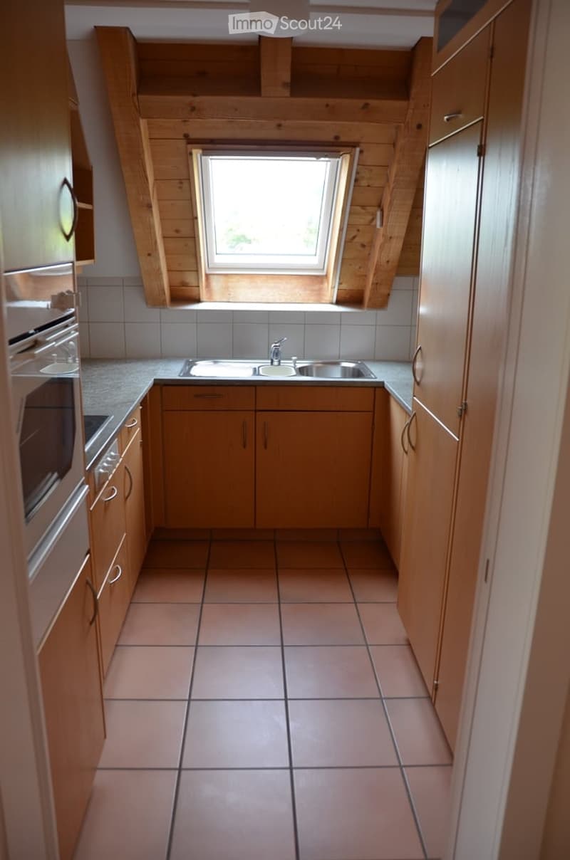Bright kitchen with wooden cabinets, tiled floor, and a window above the sink.