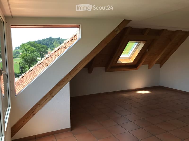 Empty room with tiled floor, white walls, wooden staircase, and skylight windows offering a view of the roof and surrounding landscape.