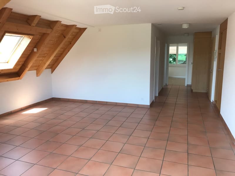 Empty room with tiled floor, white walls, and wooden beams on the ceiling. A window on the left side allows natural light to enter.