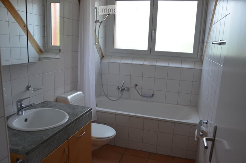 Bathroom with white tiles, a sink with a faucet, a toilet, a bathtub with a showerhead, and a mirror above the sink.
