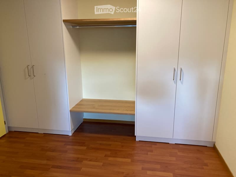 Empty closet with white built-in cabinets, wooden shelves, and a wooden floor.