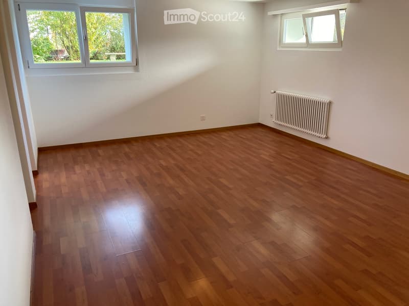 Empty room with wooden flooring, white walls, and two windows with white frames. A radiator is mounted on one wall.