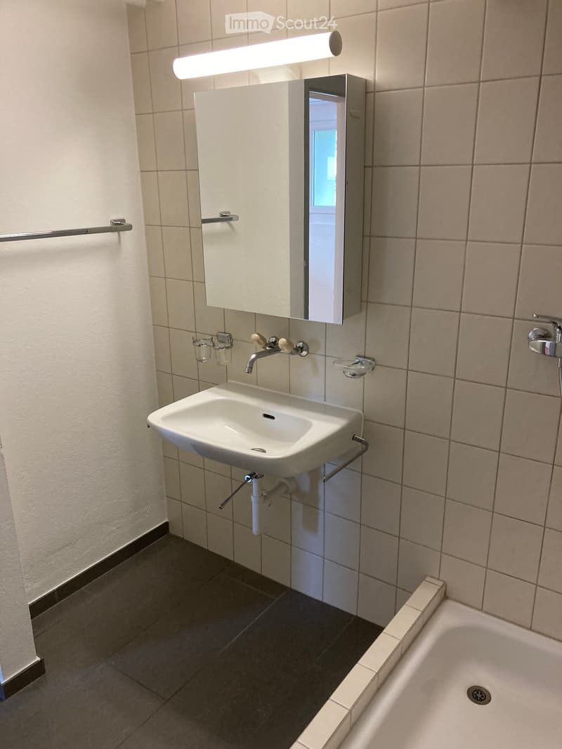 Modern bathroom with a white sink, mirror cabinet, and bathtub. Features tiled walls and floor, a faucet, and a cup holder.