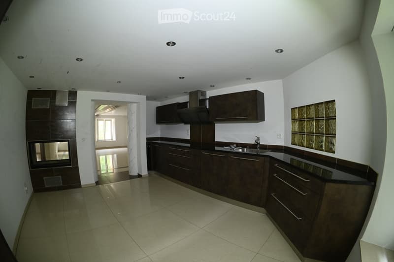 Modern kitchen with dark wooden cabinets, stainless steel sink, and a range hood. The space features tiled flooring and recessed lighting.