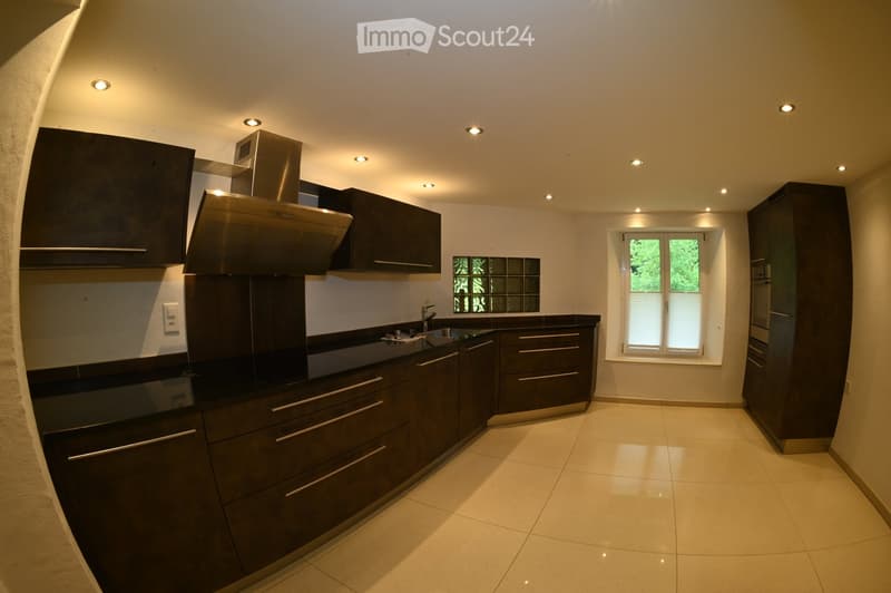 Modern kitchen with dark wooden cabinets, stainless steel range hood, black countertop, and a window with blinds.