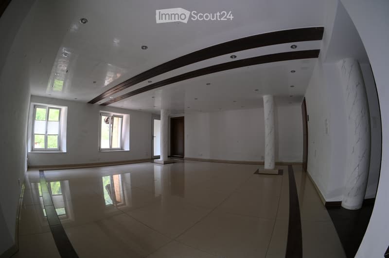 Empty room with white walls, polished tile floor, and large windows. Features include recessed lighting, decorative columns, and a wooden ceiling beam.
