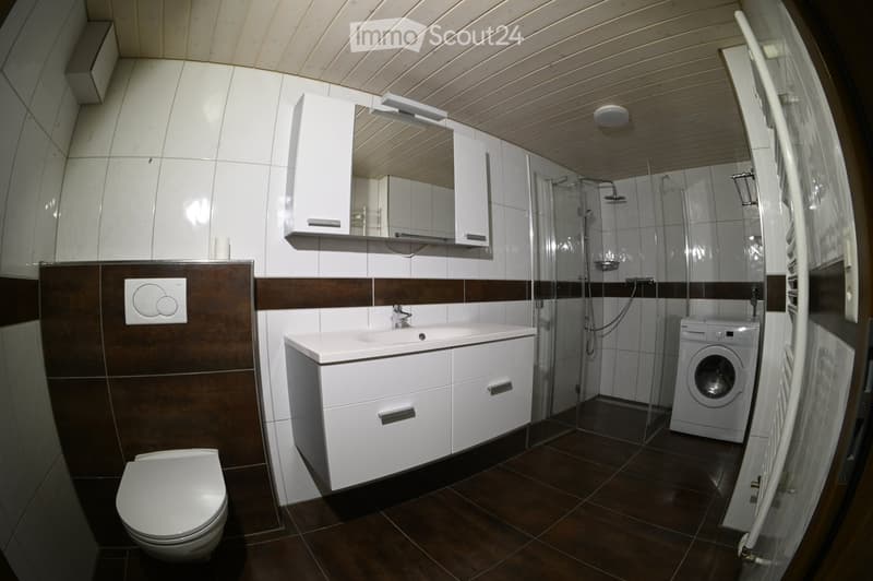 Modern bathroom with white tiles, dark brown accents, a toilet, sink, mirror, shower, and a washing machine.