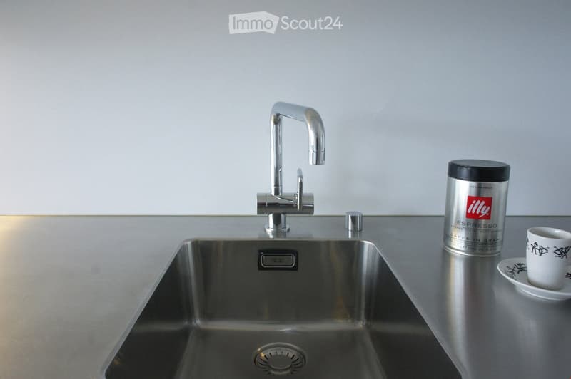 Modern kitchen sink with a sleek chrome faucet, a stainless steel sink, a white cup on a saucer, and a silver Illy Espresso can nearby.